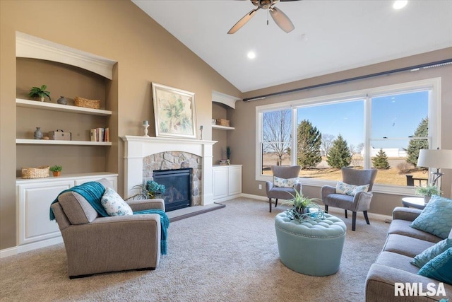 carpeted living area with a stone fireplace, built in features, a ceiling fan, and baseboards