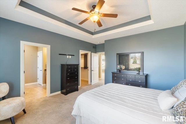 bedroom featuring a walk in closet, a tray ceiling, baseboards, and light carpet