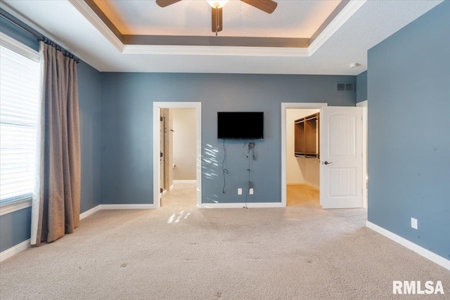 unfurnished bedroom featuring a tray ceiling, a spacious closet, carpet, and baseboards