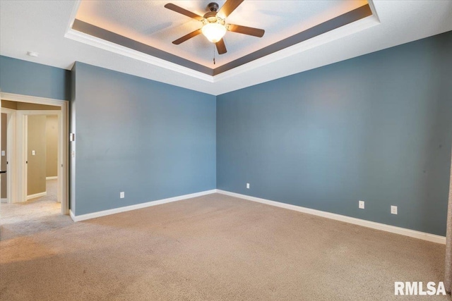 carpeted spare room with a tray ceiling, baseboards, and a ceiling fan