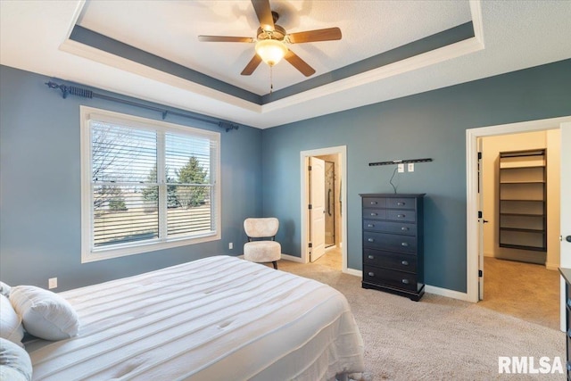 carpeted bedroom featuring a raised ceiling, baseboards, ensuite bathroom, and ceiling fan