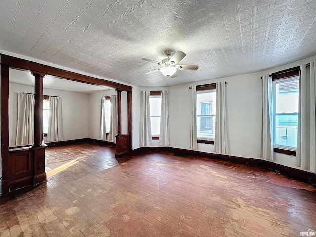 empty room featuring ceiling fan, wood-type flooring, and ornate columns