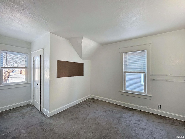 additional living space with vaulted ceiling, dark colored carpet, and a textured ceiling