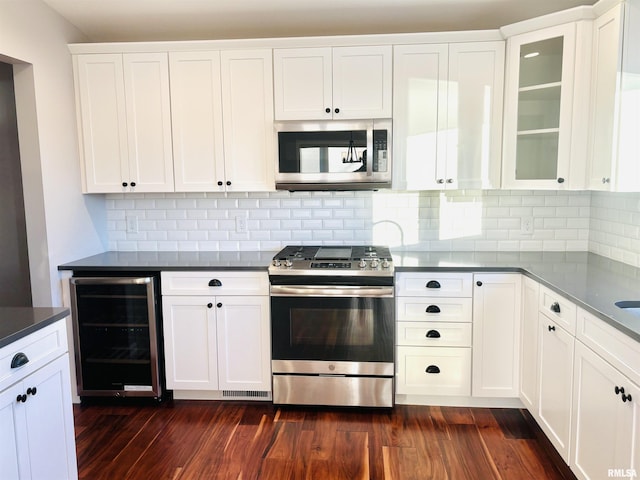 kitchen with white cabinets, appliances with stainless steel finishes, tasteful backsplash, dark hardwood / wood-style flooring, and beverage cooler