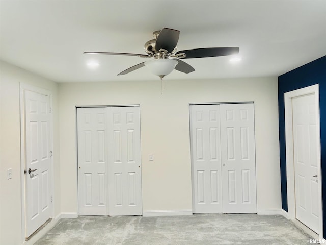 unfurnished bedroom with two closets, ceiling fan, and light colored carpet