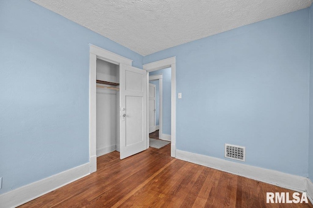 unfurnished bedroom featuring dark hardwood / wood-style floors, a textured ceiling, and a closet