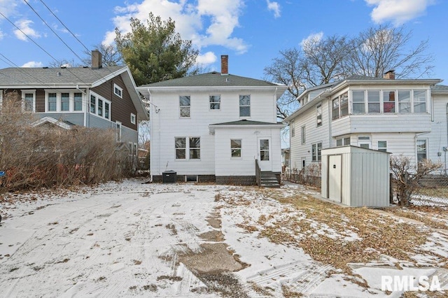 snow covered rear of property featuring a storage shed