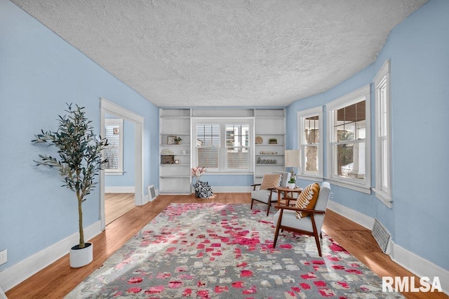 sitting room featuring built in shelves, a textured ceiling, light hardwood / wood-style floors, and plenty of natural light