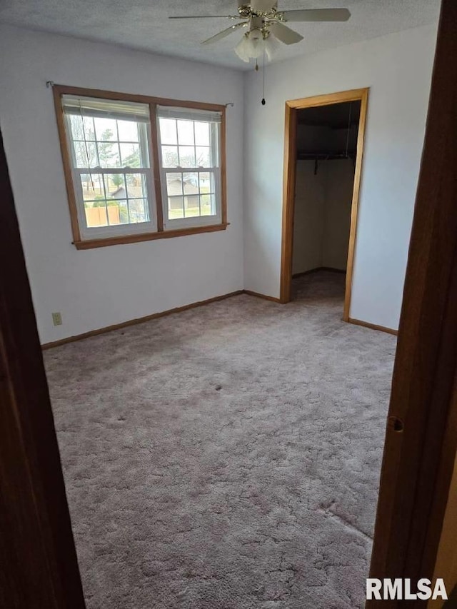 unfurnished bedroom with a closet, a walk in closet, light colored carpet, and ceiling fan