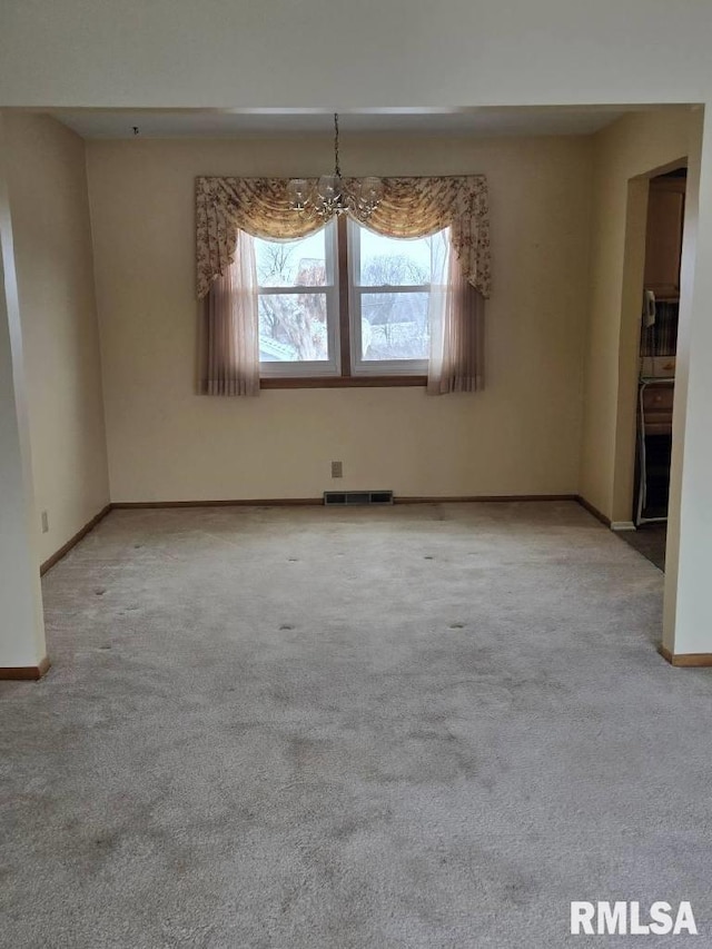 empty room featuring a notable chandelier and light carpet