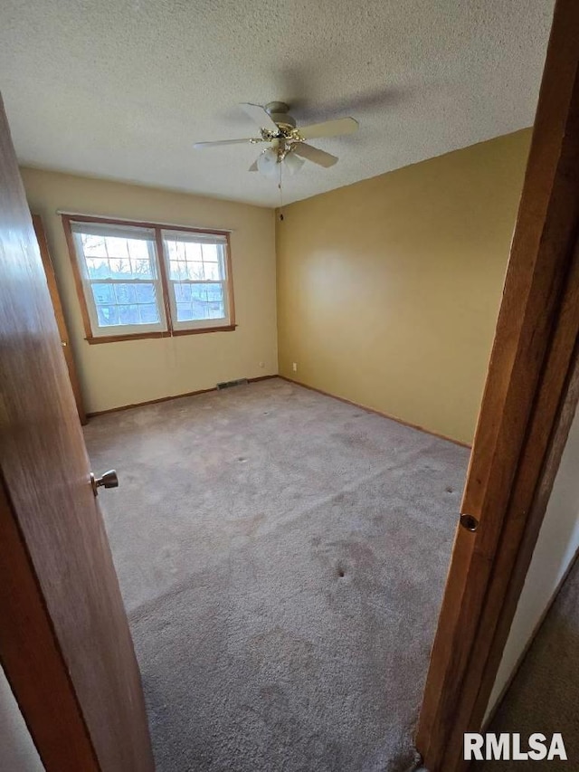 unfurnished room with ceiling fan, a textured ceiling, and light carpet