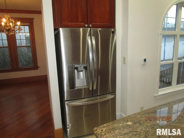 kitchen featuring baseboards, dark stone countertops, wood finished floors, stainless steel refrigerator with ice dispenser, and a notable chandelier