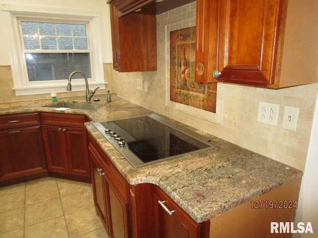 kitchen with decorative backsplash, a sink, black electric stovetop, and light stone countertops