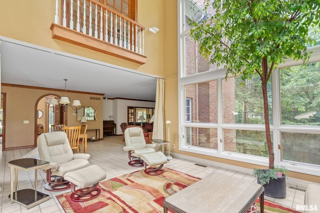 tiled living room featuring a high ceiling, an inviting chandelier, and ornamental molding