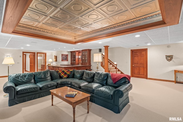 carpeted living room featuring a raised ceiling, decorative columns, crown molding, and indoor bar