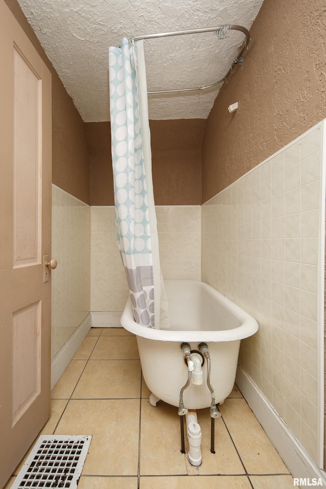 bathroom with tile patterned flooring, tile walls, a tub to relax in, and a textured ceiling