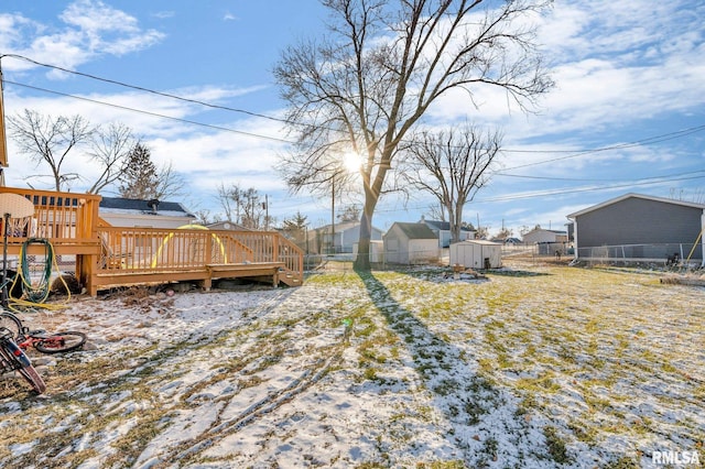 snowy yard featuring a storage unit and a wooden deck