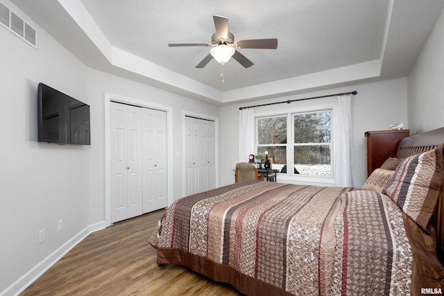 bedroom with hardwood / wood-style flooring, a raised ceiling, and ceiling fan