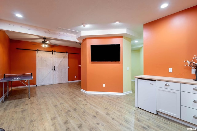 interior space featuring light wood-type flooring, beam ceiling, a barn door, and ceiling fan