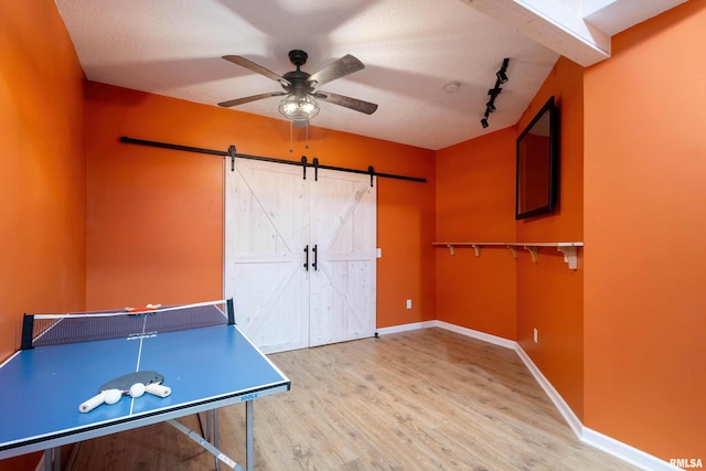 recreation room featuring rail lighting, a textured ceiling, ceiling fan, a barn door, and light hardwood / wood-style floors