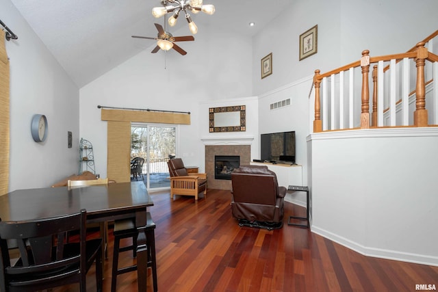 dining area featuring ceiling fan, a towering ceiling, dark wood-type flooring, and a tile fireplace