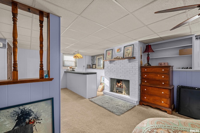 living room featuring a paneled ceiling, ceiling fan, light colored carpet, and a brick fireplace