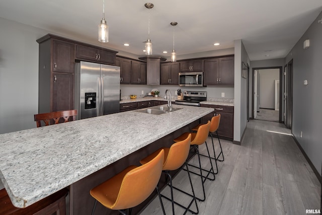 kitchen featuring sink, light hardwood / wood-style floors, decorative light fixtures, a kitchen island with sink, and appliances with stainless steel finishes