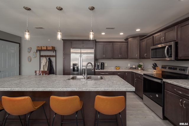 kitchen featuring dark brown cabinetry, sink, an island with sink, and stainless steel appliances