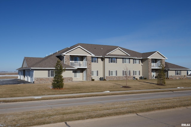 view of front of property featuring a balcony, central AC unit, and a front yard