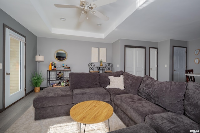 living room with a tray ceiling, ceiling fan, and light hardwood / wood-style floors