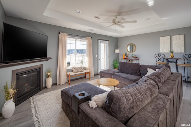 living room featuring a tray ceiling, ceiling fan, and light hardwood / wood-style floors