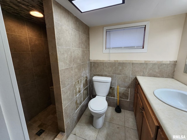 bathroom featuring vanity, a shower, tile patterned floors, toilet, and tile walls