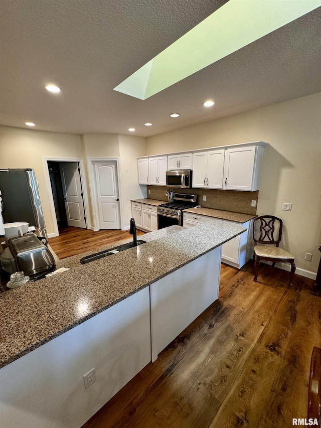 kitchen with a skylight, dark stone counters, stainless steel appliances, sink, and white cabinets