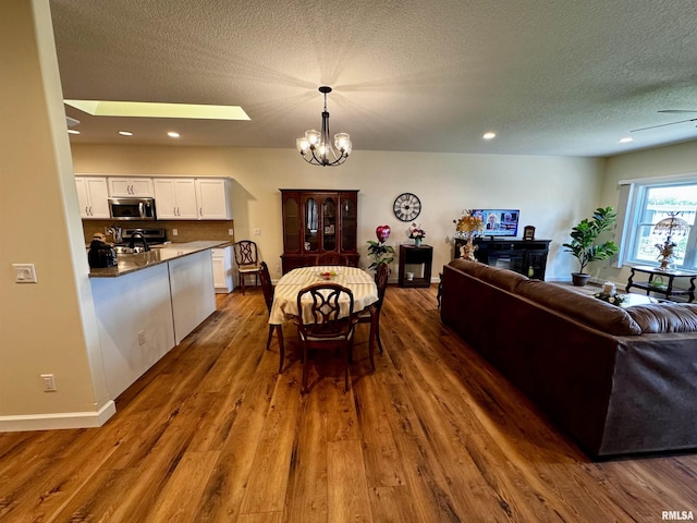 dining area featuring a textured ceiling, ceiling fan with notable chandelier, dark wood-type flooring, and a skylight