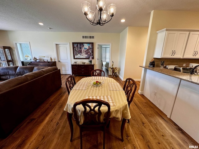 dining room with dark hardwood / wood-style flooring, a textured ceiling, and an inviting chandelier