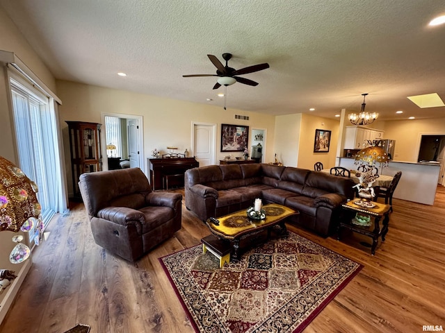 living room featuring ceiling fan with notable chandelier, hardwood / wood-style floors, a textured ceiling, and a skylight