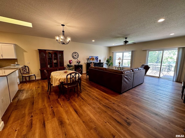 dining area with ceiling fan with notable chandelier, a textured ceiling, and dark hardwood / wood-style floors