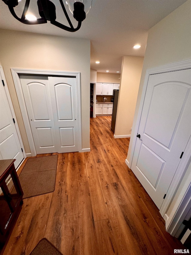 corridor featuring light wood-type flooring and a notable chandelier