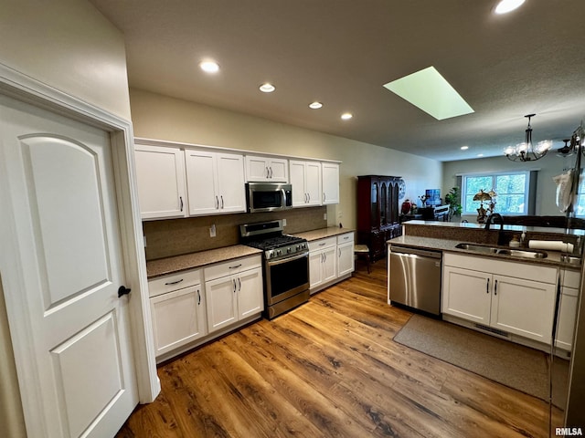 kitchen featuring appliances with stainless steel finishes, backsplash, a skylight, sink, and white cabinets