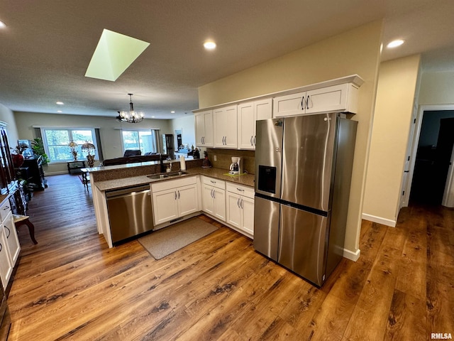 kitchen with sink, kitchen peninsula, hanging light fixtures, appliances with stainless steel finishes, and white cabinetry