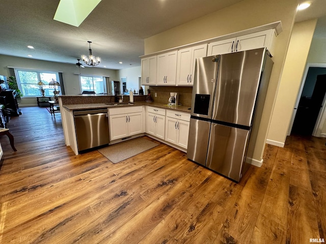 kitchen with decorative light fixtures, a notable chandelier, white cabinetry, kitchen peninsula, and stainless steel appliances