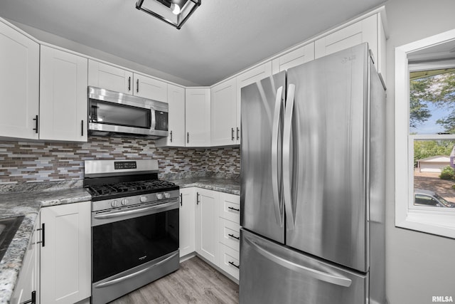 kitchen featuring white cabinets, appliances with stainless steel finishes, tasteful backsplash, and dark stone countertops