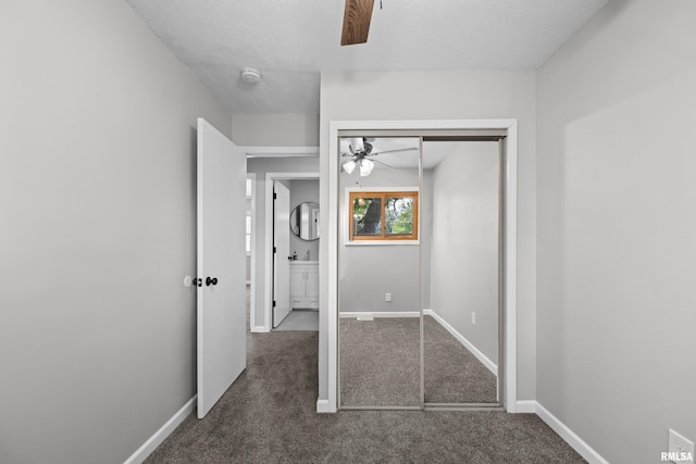 unfurnished bedroom with dark colored carpet, ceiling fan, a textured ceiling, and a closet