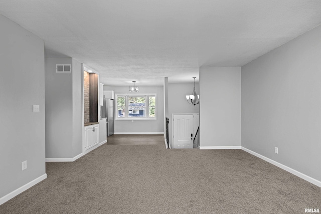 unfurnished living room featuring a textured ceiling, dark carpet, and a notable chandelier