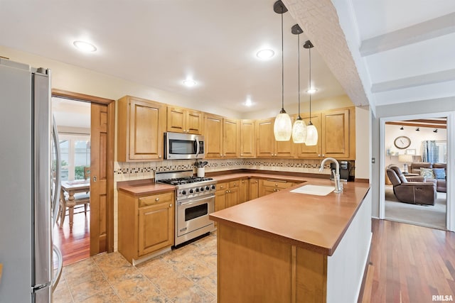 kitchen featuring a peninsula, backsplash, stainless steel appliances, pendant lighting, and a sink