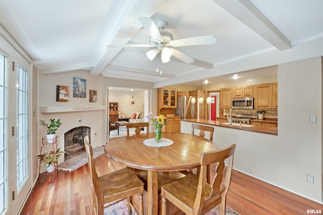 dining area featuring a fireplace, light wood-style flooring, and beamed ceiling