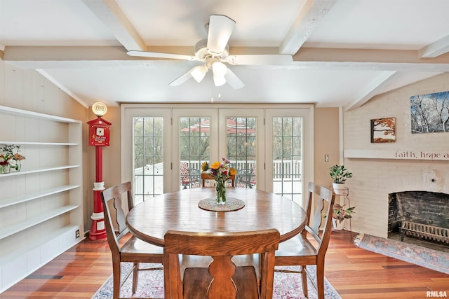 dining area with built in features, ceiling fan, a fireplace, wood finished floors, and vaulted ceiling with beams