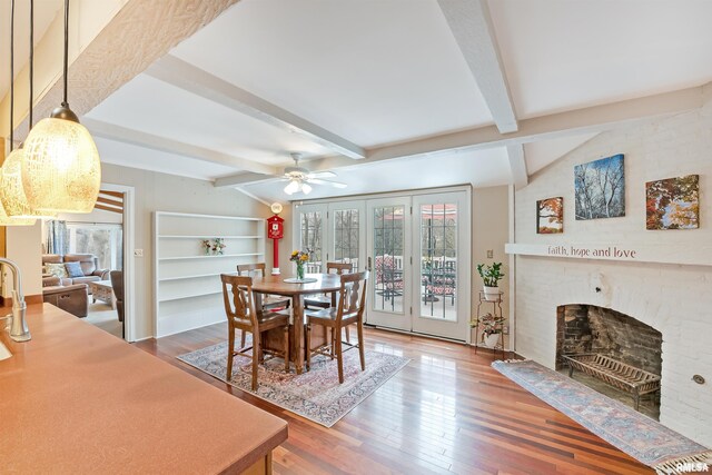 dining room featuring ceiling fan, vaulted ceiling with beams, a brick fireplace, and wood finished floors
