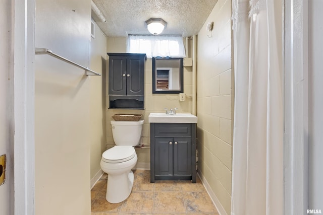 bathroom with toilet, a textured ceiling, vanity, and concrete block wall