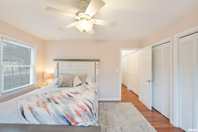 bedroom with two closets, wood finished floors, ceiling fan, and baseboards